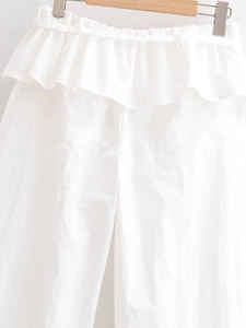 Détail d'un pantalon blanc à taille haute et jambe large avec taille plissée à volants
