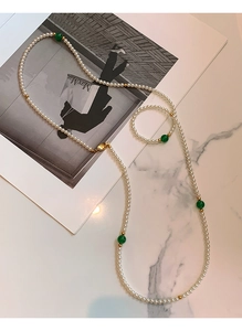 Flat lay of a long pearl necklace with green beads on a marble surface and fashion magazine