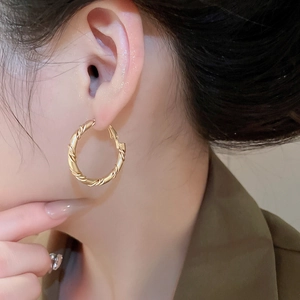 Close-up of gold twisted rope texture hoop earrings worn by a model in a side view