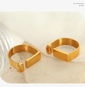 Detail of minimalist gold-plated adjustable open rings on textured stone and fabric background