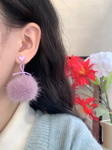 Detail of purple faux fur pompom earrings with heart studs worn on a model side view