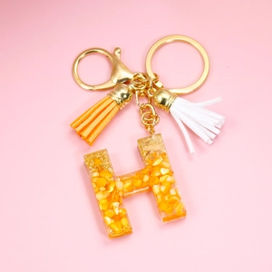 Close-up of golden letter H keychain with orange resin, corn kernels and colorful tassels