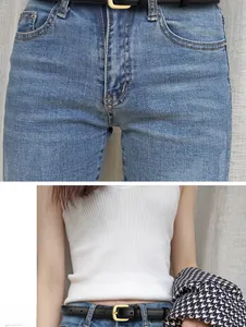 Detail of slim black leather belt with gold buckle on blue jeans and knit top