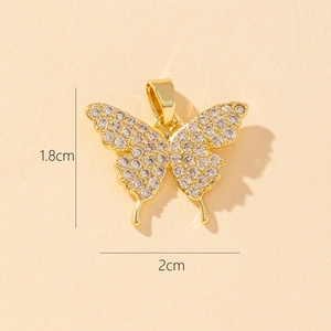Detailed close-up of a 2cm gold butterfly pendant with sparkling cubic zirconia on beige paper