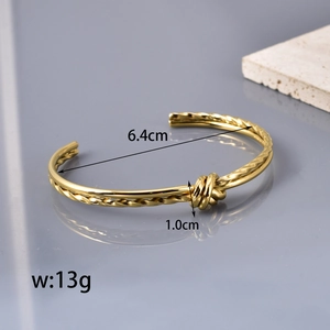 Polished gold stainless steel knot cuff bracelet with twisted design on grey background