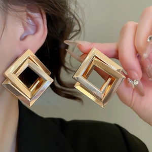 Close-up of oversized geometric double square gold earrings with a polished mirror finish