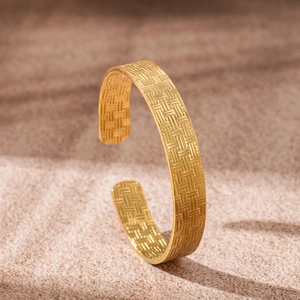 Detail of 18K gold-plated stainless steel cuff with intricate woven texture on sand