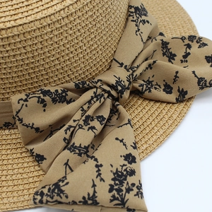 Detail of hand-woven straw sun hat featuring a floral bow ribbon and premium fiber texture