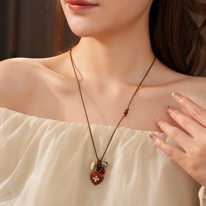 Detail of bohemian necklace with red heart stone, silver cross and wax rope on a model