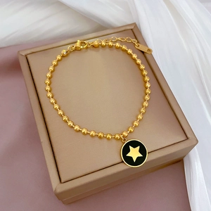 Dettaglio bracciale a sfere dorate con ciondolo a stella nera su scatola per gioielli