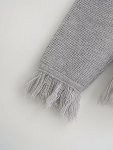 Close-up of grey knit cardigan featuring delicate fringe tassels on the cuffs