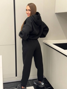 Side view of black fleece hoodie set showing casual fit in a minimalist kitchen setting
