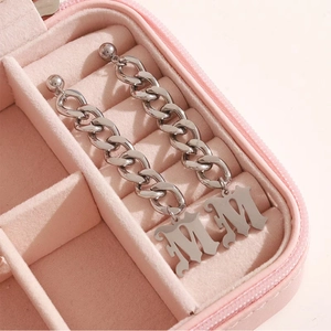 Boucles d'oreilles chaîne argentées avec pendentifs M dans un écrin en velours rose