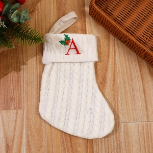 White knit Christmas stocking with red letter A embroidery on wooden floor with pine decor