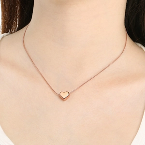 Gros plan d'un pendentif cœur minimaliste en or rose sur une fine chaîne serpent élégante