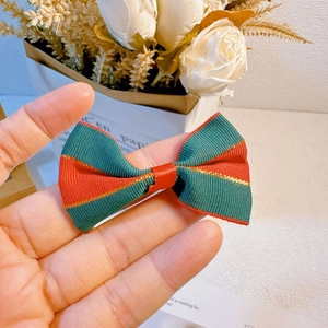 Detail of red and green striped Christmas bow with gold trim held against white background