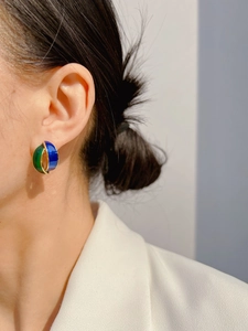 Close-up of model wearing geometric blue and green enamel earrings with gold trim