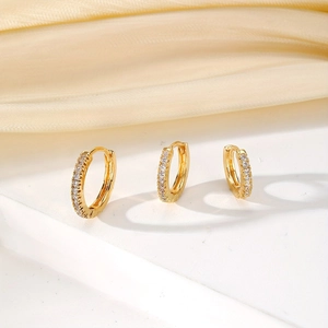 Three-piece gold plated huggie earrings set with sparkling zircon pavé on white podium