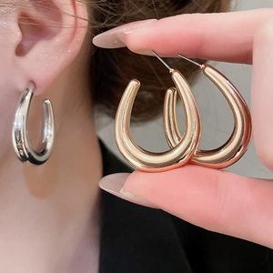 Close-up of polished U-shaped hoop earrings in gold and silver finish on a model