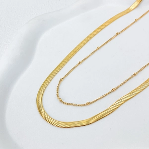 Detail of double-layer gold snake chain and beaded necklace on a white display tray