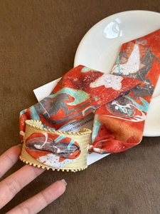 Macro view of vintage orange printed silk scarf intertwined with textured gold metal cuff
