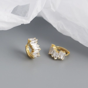 Close-up of gold hoop earrings with rectangular cubic zirconia stones on white paper