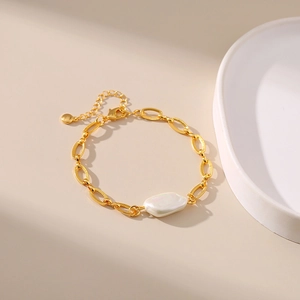 Detail of gold chain bracelet with irregular pearl and lobster clasp on beige setting