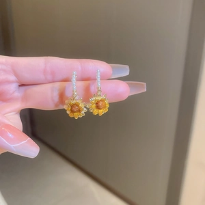 Close-up of sunflower earrings with yellow petals and delicate pearl-studded C-shaped hooks