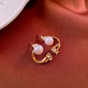 Elegant C-shaped gold pearl earrings with sparkling zircons on clay textured fabric
