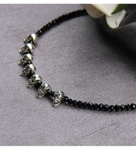 Detail of gothic black beaded necklace with silver skull charms on grey background