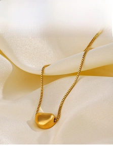 Detailed macro view of a polished gold bean pendant on a delicate box chain necklace