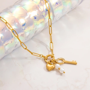 Close-up of golden necklace with heart charm, rhinestone key and white pearls