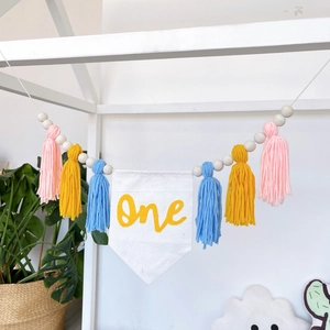 Close-up of birthday high chair banner with One print, pastel tassels and wooden beads