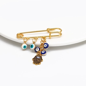 Detail of a golden Hamsa Hand brooch with multiple evil eye charms on a white plate