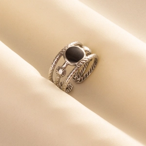 Close-up of silver twisted rope ring with a black circular inlay on beige fabric