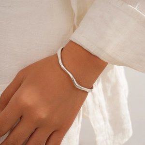 Detail view of silver wavy geometric open cuff bracelet on female wrist with warm lighting
