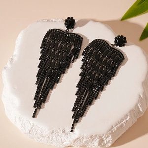 Détail de boucles d'oreilles à pompons noirs avec fleurs en zircon sur socle en pierre