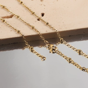 Detail of gold beaded chain necklace over beige stone and reflective mirror surface