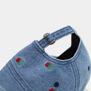 Macro detail of cherry embroidery on washed denim baseball cap with adjustable metal buckle