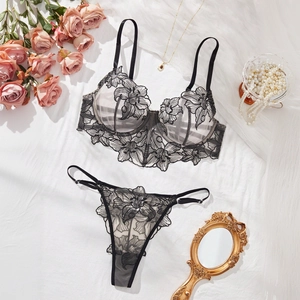 Flat lay of black floral lace embroidery lingerie set with pearls and rose petals