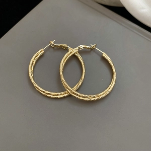Detail view of gold twist hoop earrings with textured spiral design on a gray matte surface