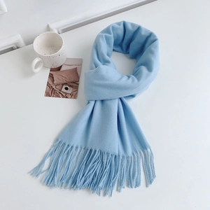 Detailed flat lay of blue cashmere-like scarf with fringe on a minimalist white desk
