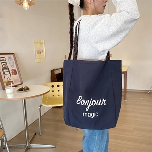 Navy blue large tote bag with Bonjour print worn by a model in a minimalist cafe