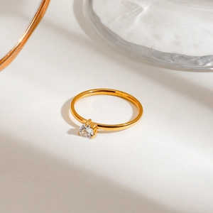 Detail of a minimalist gold ring with a sparkling pear-cut clear gemstone in a prong setting