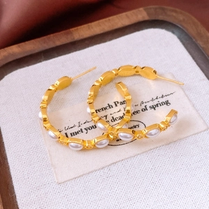 Macro detail of 18K gold plated C-shaped hoop earrings with pearls on white linen