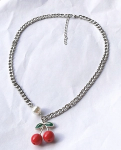 Detail of silver Cuban chain necklace with red cherry pendant and white pearl bead