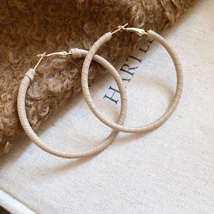 Close-up of geometric hoop earrings featuring gold metal wrapped in beige leather