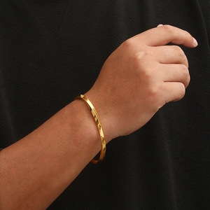 Detail view of a golden Mobius twisted cuff bracelet on a person's wrist with black fabric