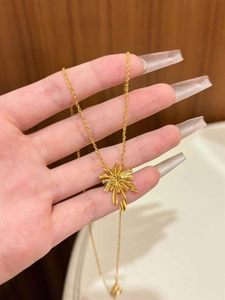 Detail of hand-held gold plated floral necklace featuring a firework leaf pendant