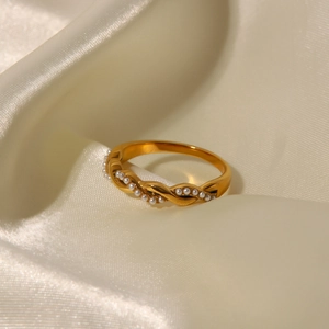 Twisted titanium steel ring in gold finish with delicate pearl inlays on beige silk